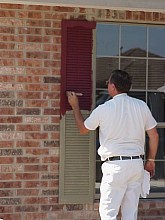 The painter applies the first coat of paint to the shutters.